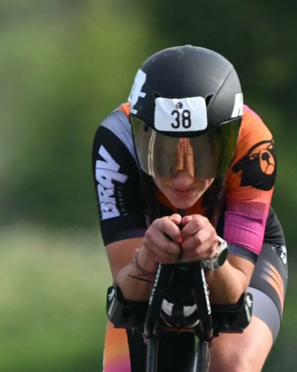 A cyclist racing a time trial in an aero tuck on a country road
